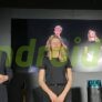 dyson - funzionalità Presentatore e partecipanti a evento tech, con dispositivo di tecnologia avanzata in primo piano, con grande schermo sullo sfondo, in un ambiente moderno e professionale.