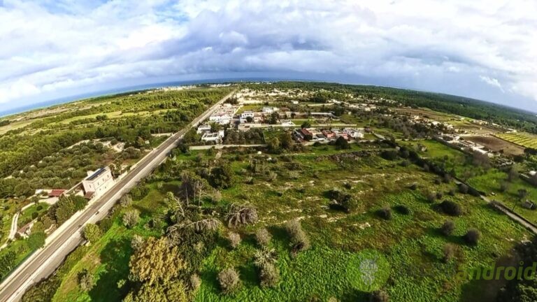 Paesaggio rurale dall'alto con campi verdi, strade e case. Veduta panoramica di un'area agricola con vegetazione estesa e cielo nuvoloso, perfetta per notizie di tecnologia e lifestyle. Paesaggio rurale con campi verdi, case e strade, vista dall'alto, cielo nuvoloso, scenario naturale e tranquillo, ideale per contenuti tecnologici e innovativi di TecnoAndroid.