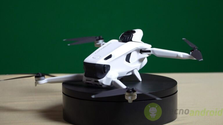 Drone bianco con telecamera, tecnologia avanzata, fotografia aerea, gadget innovativo, drone con sgancio funzionante, tecnologia droni, videomaking, riprese aeree, novità tecnologiche, TecnoAndroid. Drone bianco con quattro eliche su base nera, posizionato su un supporto nero, utilizzato per riprese aeree e fotografia con notevoli funzionalità di stabilità e controllo.