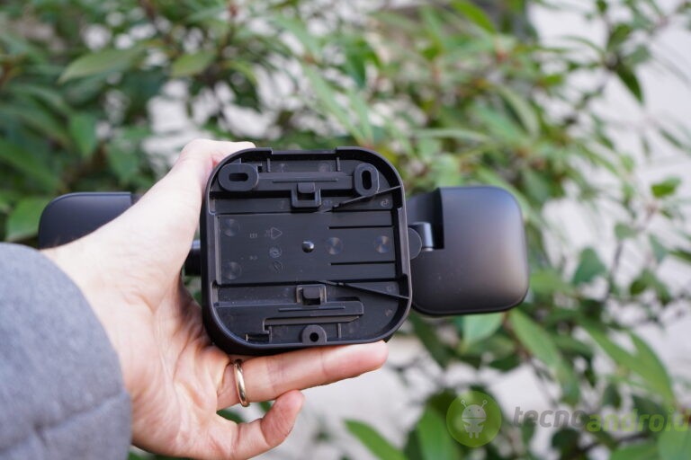 blink - immagine 12 Immagine di una mano che tiene un dispositivo Bluetooth con area verde di piante sullo sfondo, evidenziando accessori tecnologici e connettività.