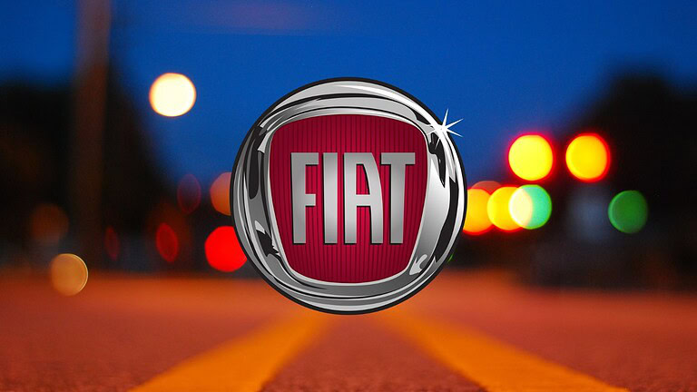 Logo Fiat su sfondo di notte con luci colorate e effetto bokeh. Immagine che evidenzia il marchio Fiat, simbolo di auto italiane, in un contesto urbano notturno per contenuti su automobili, tecnologia e veicoli italiani.