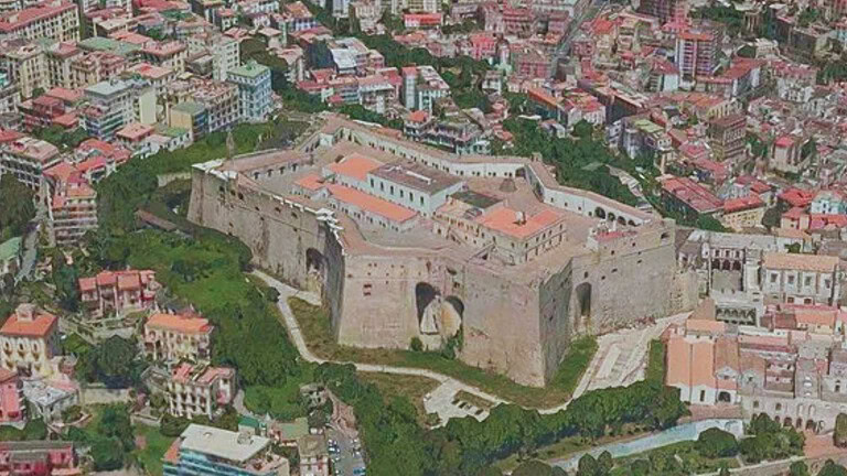 Immagine di una vista aerea della fortezza di Alghero, con le sue imponenti mura storiche e le abitazioni circostanti con tetti rossi, che evidenziano il fascino storico e il paesaggio urbano della città sarda. Perfetta per contenuti su turismo, storia e cultura di Alghero.