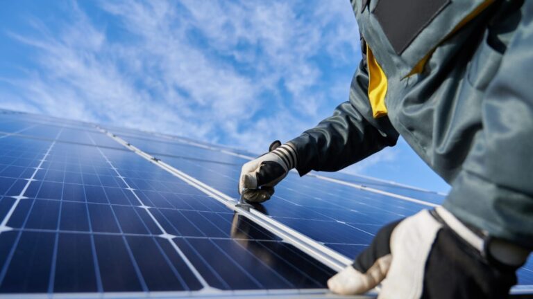 Immagine di un operatore che installa pannelli solari fotovoltaici sotto un cielo blu, evidenziando l'importanza delle energie rinnovabili.