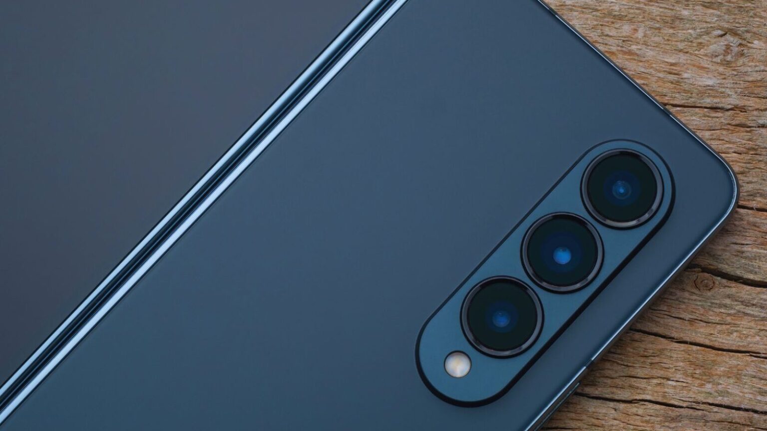 Alt text: Telefono intelligente con modulo fotocamera triplo, dettagli accurati e design elegante su superficie di legno, ideale per appassionati di tecnologia e fotografia.