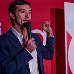 Presentatore durante evento tecnologico con schermo pubblicitario.