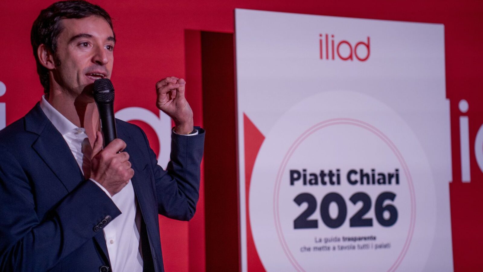 iliad piatti chiari Presentatore durante evento tecnologico con schermo pubblicitario.