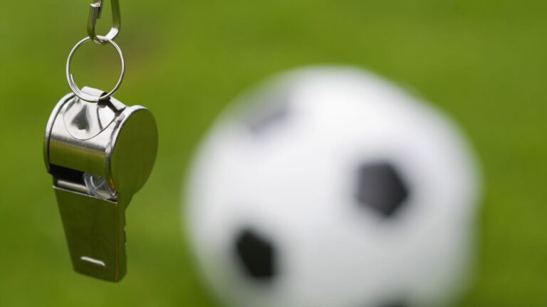 Fischietto da arbitro e pallone da calcio in campo verde.