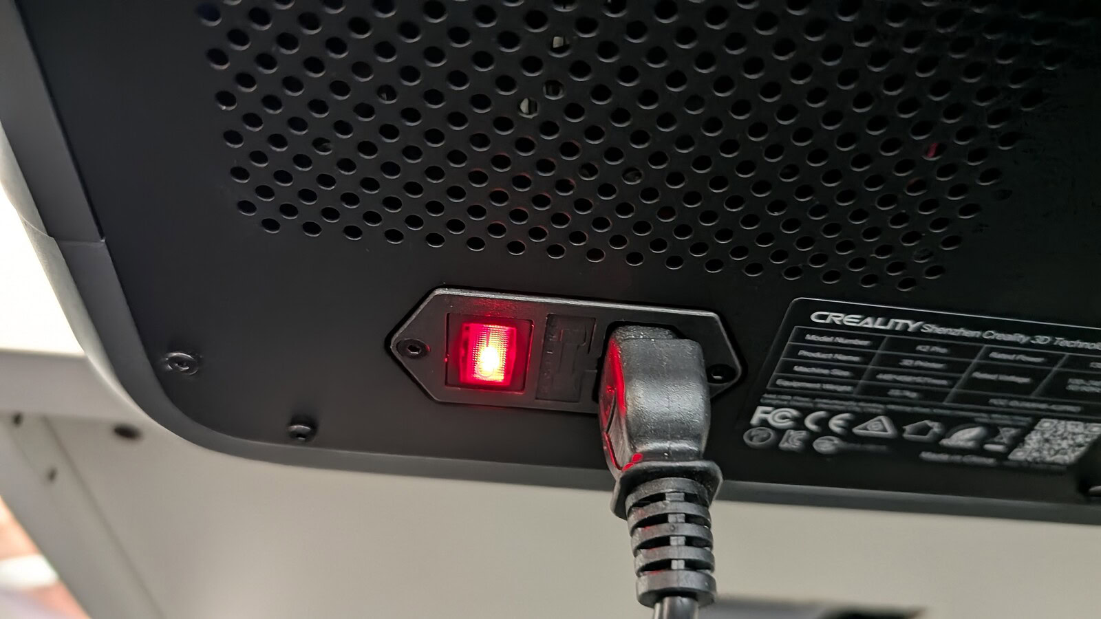 Creality K2 Pro Combo - immagine 18 Testo alternativo: Immagine di una presa di corrente con cavo collegato, illuminata da luce rossa, situata sul retro di un dispositivo tecnologico.