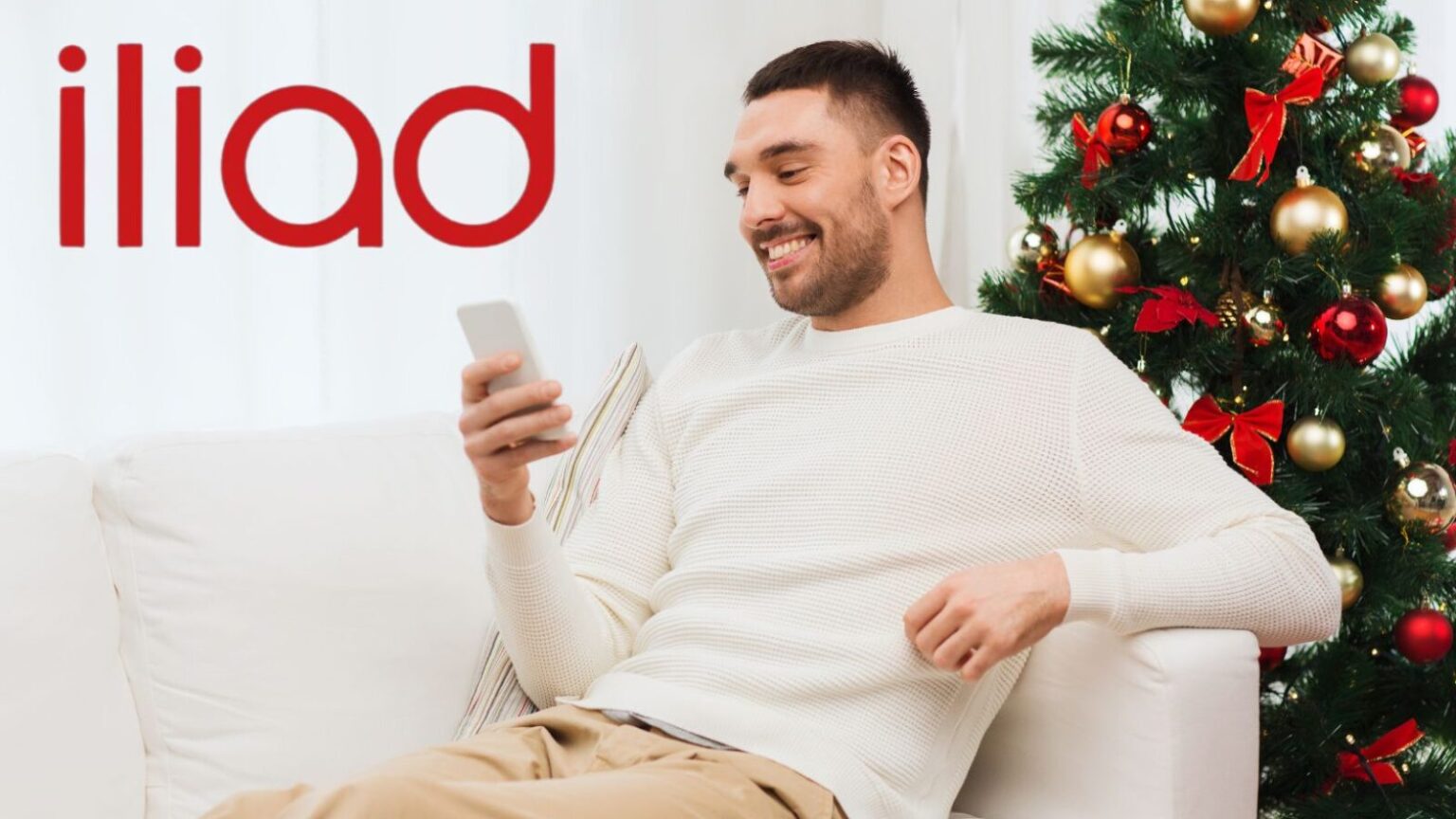 Uomo felice con smartphone davanti all'albero di Natale decorato con palline e nastri rossi, atmosfera di festa, tecnologia, regali e convivialità, ideale per articoli su tech e festività.