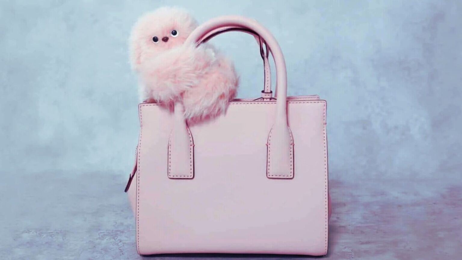 Pupazzo di peluche soffice e carino appoggiato su una borsa rosa, ideale come accessorio decorativo o regalo, perfetto per appassionati di moda e oggetti originali.