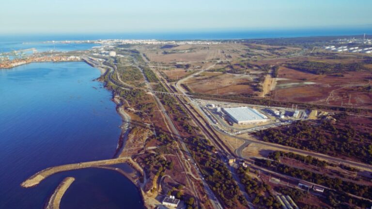 Vista panoramica della costa e delle opere portuali, con vaste aree industriali e zone verdi, evidenziando le tecnologie e le innovazioni nel settore marittimo e infrastrutturale in un ambiente di alta tecnologia.