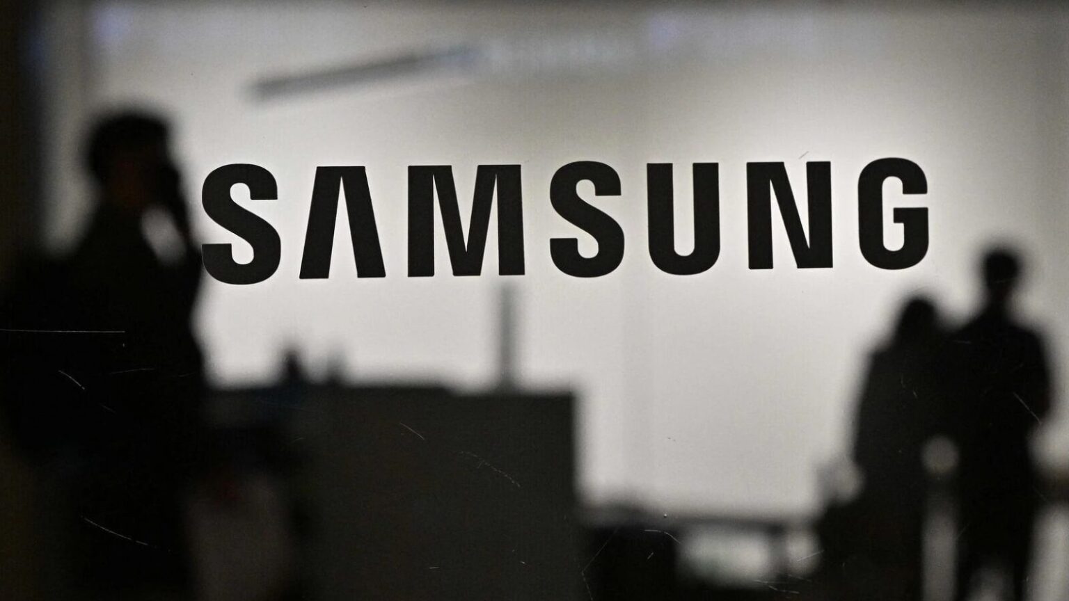 Immagine con logo Samsung sfocato, persone al lavoro, ambiente tecnologico, innovazione, dispositivi Samsung, alta qualità, prodotti di elettronica, smartphone, tecnologia all'avanguardia, digitale.