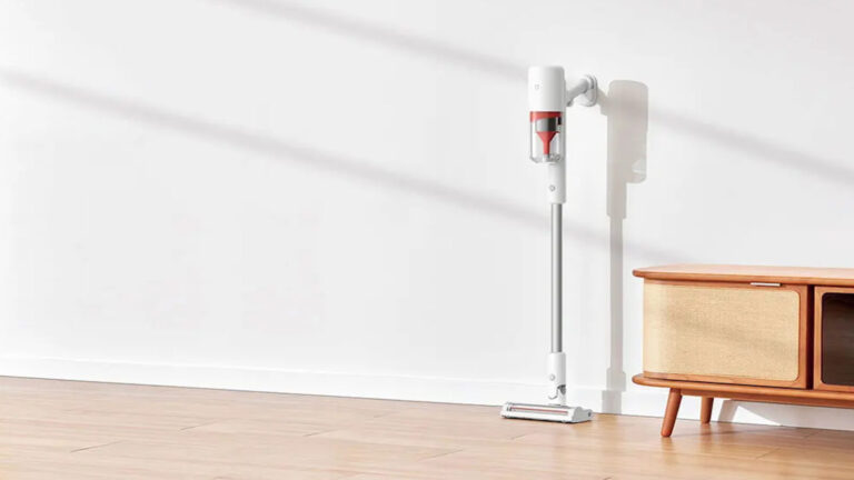 Aspirapolvere senza filo bianco e rosso in soggiorno con pavimento di legno e mobile legno chiaro, design minimalista, ideale per pulizie rapide e efficaci.